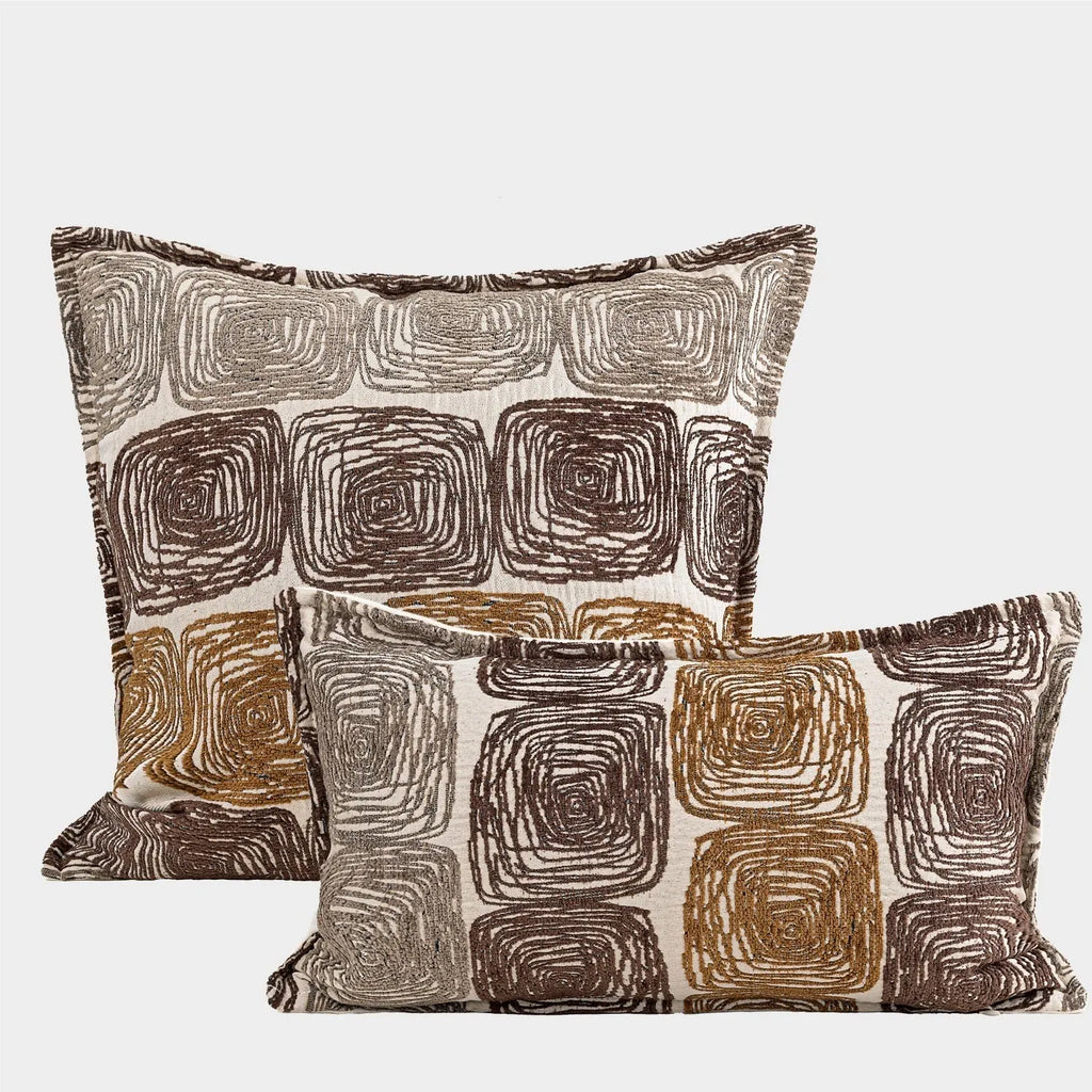 Cream and coffee-coloured abstract coil pattern square pillow cover 50x50cm on a grey sofa.