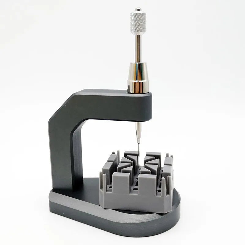 Silver tool steel press strap removal tool for watch bands and jewellery on a grey background.
