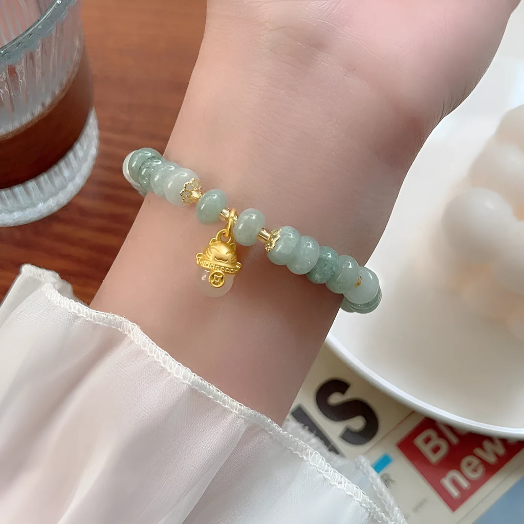Women's lucky cat bracelet made from strung strawberry quartz or grey jade stones with zodiac charms.