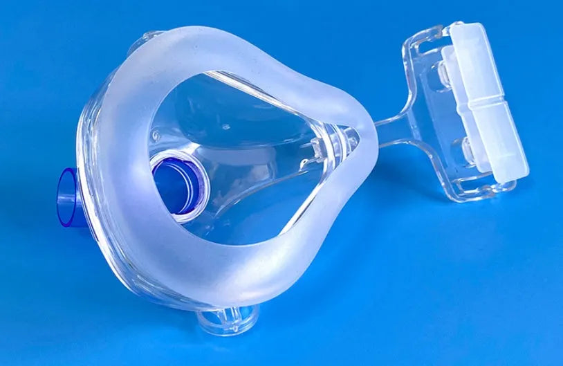 Transparent silicone CPAP breathing mask with headgear and two rotary adapter elbows on a white background.
