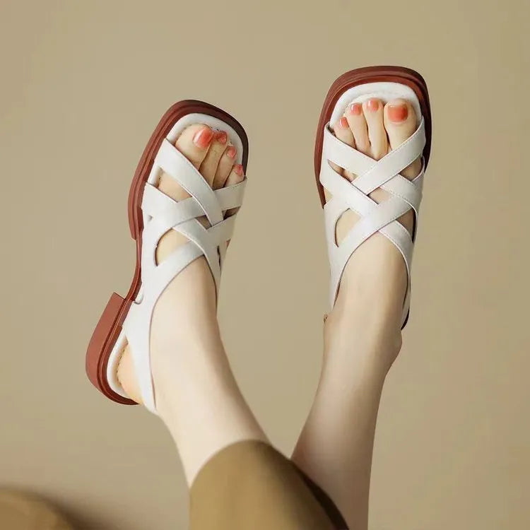 Women's glossy black patent leather sandals with square toe and cross-belt fastening on a light background.