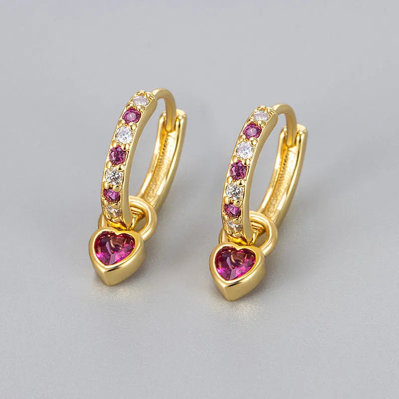 Close-up of women's fashion clip-on earrings with a heart-shaped pink cubic zirconia stone in a gold-coloured copper setting.