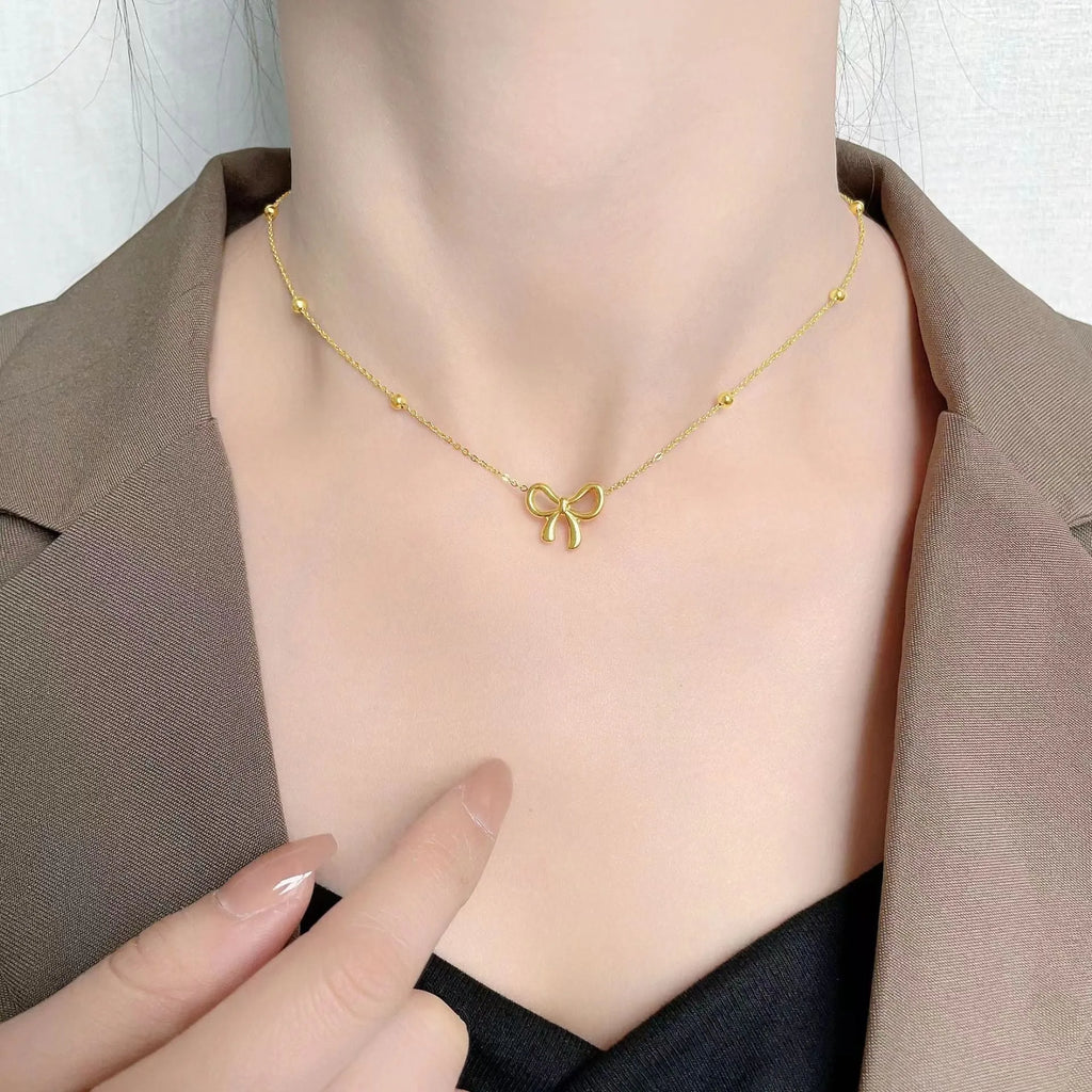 Gold coloured bow pendant necklace on a cross chain, showing adjustable length.