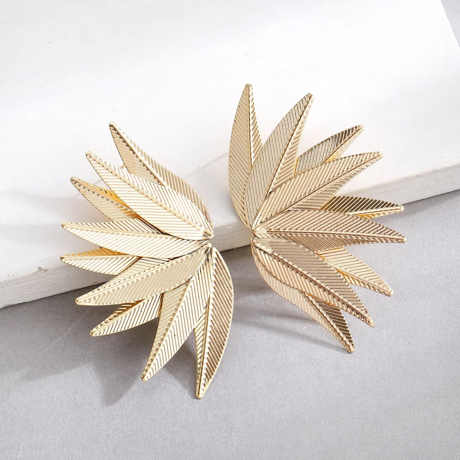 A pair of gold and white alloy patch earrings shaped like leaves.