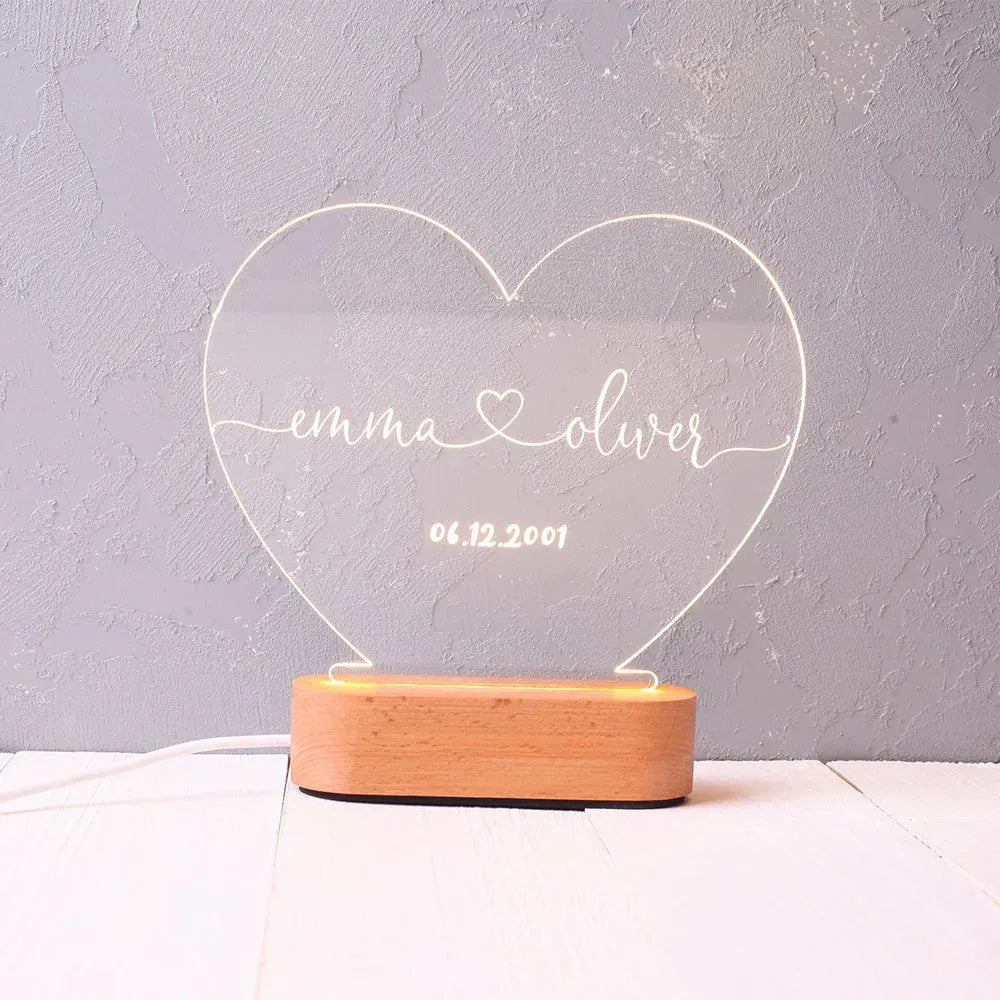 Custom transparent acrylic LED night light engraved with personal names and a date on a bedside table.