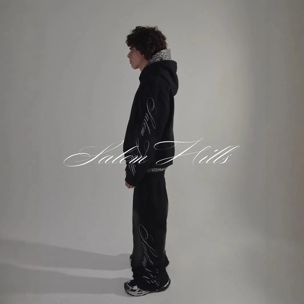 Man wearing a black punk-print hooded pullover jumpsuit with long sleeves and fleece lining.
