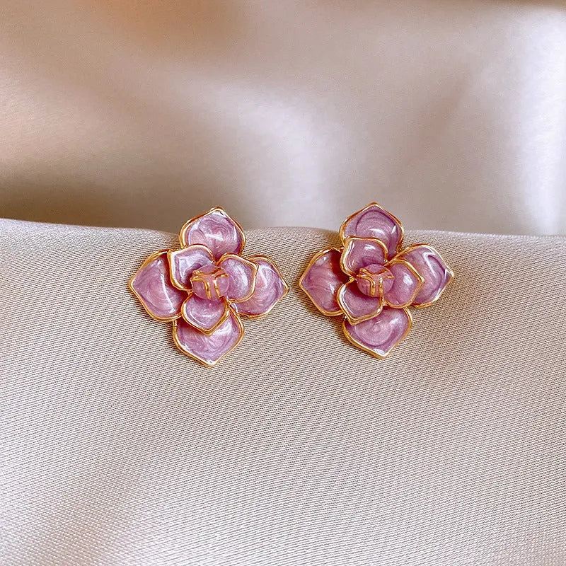 A pair of gold-plated purple floral stud earrings with silver needle details on a white background.