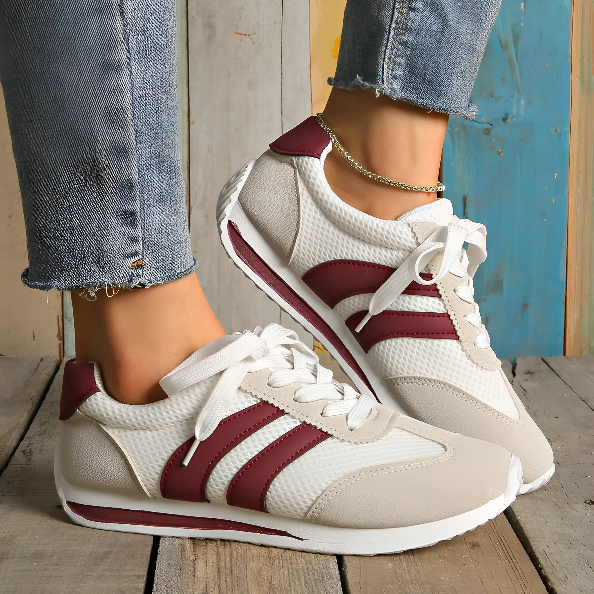 Wine red women's low-top sneaker with mesh upper, synthetic leather accents, and elastic cross straps on a flat rubber sole.