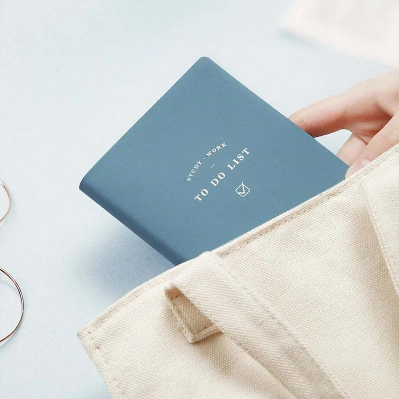 A simple portable todolist notebook in morandi blue with a PU cover, shown next to a pen.
