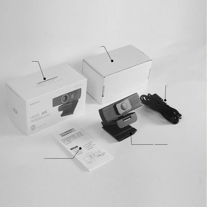 Black USB computer webcam with a magnetic privacy cover on a desk next to a laptop