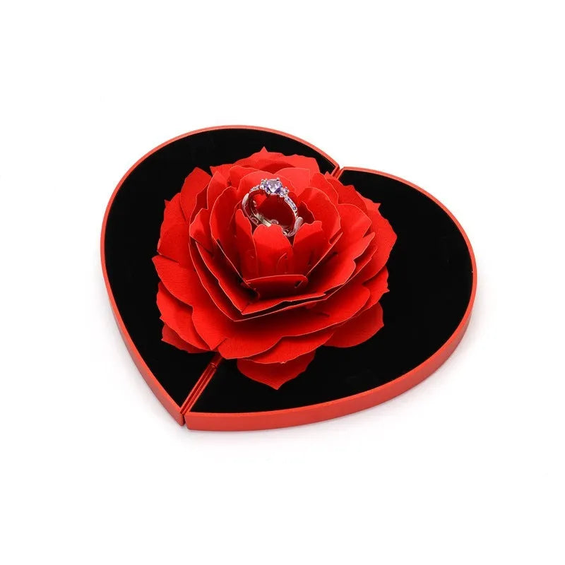 Red heart-shaped plastic ring box on a white background, showing its rotating mechanism.