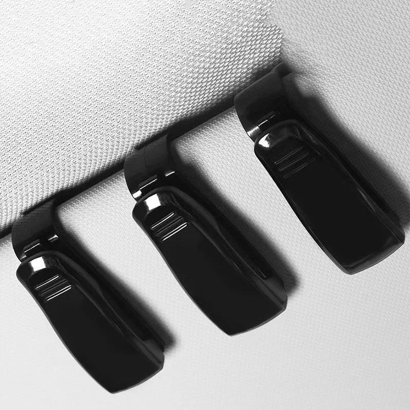 Black plastic clip mounted on a car sun visor holding a pair of sunglasses and an ID card.
