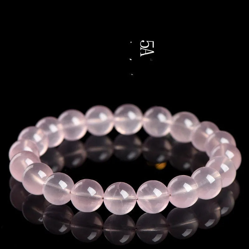 A pink natural crystal bead bracelet with polished round beads in a single circle design on a wrist.