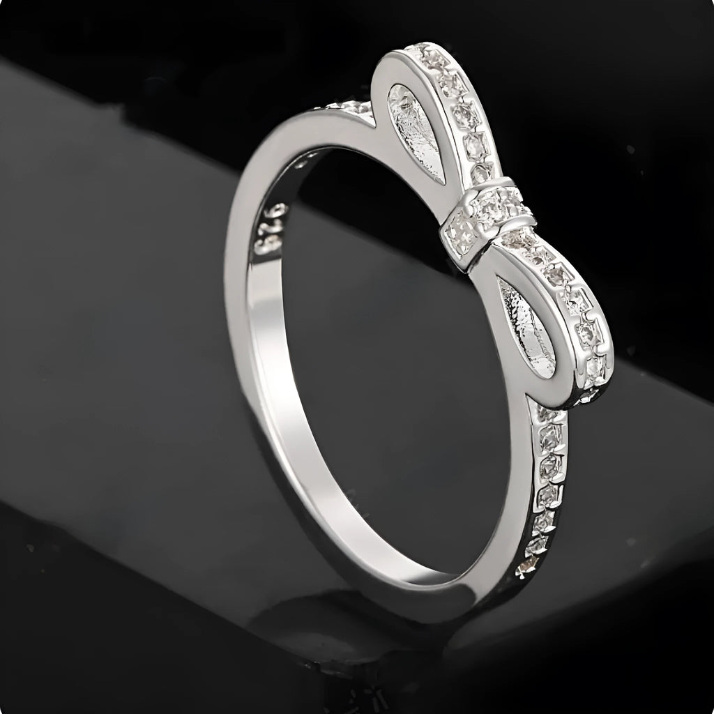 Silver coloured bow-shaped ring with rhinestone and zircon crystal decoration on a model's finger.