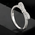 Silver coloured bow-shaped ring with rhinestone and zircon crystal decoration on a model's finger.