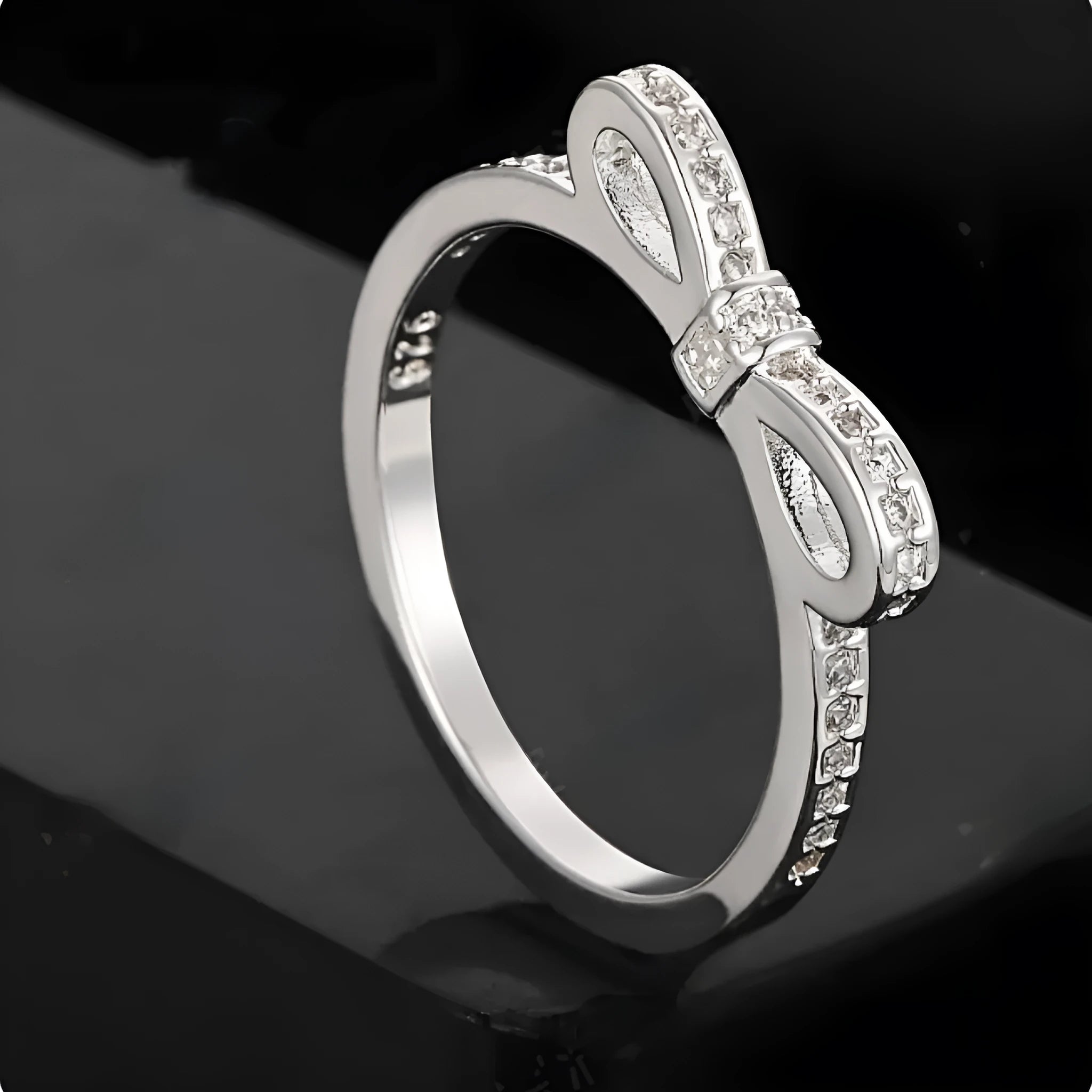 Silver coloured bow-shaped ring with rhinestone and zircon crystal decoration on a model's finger.