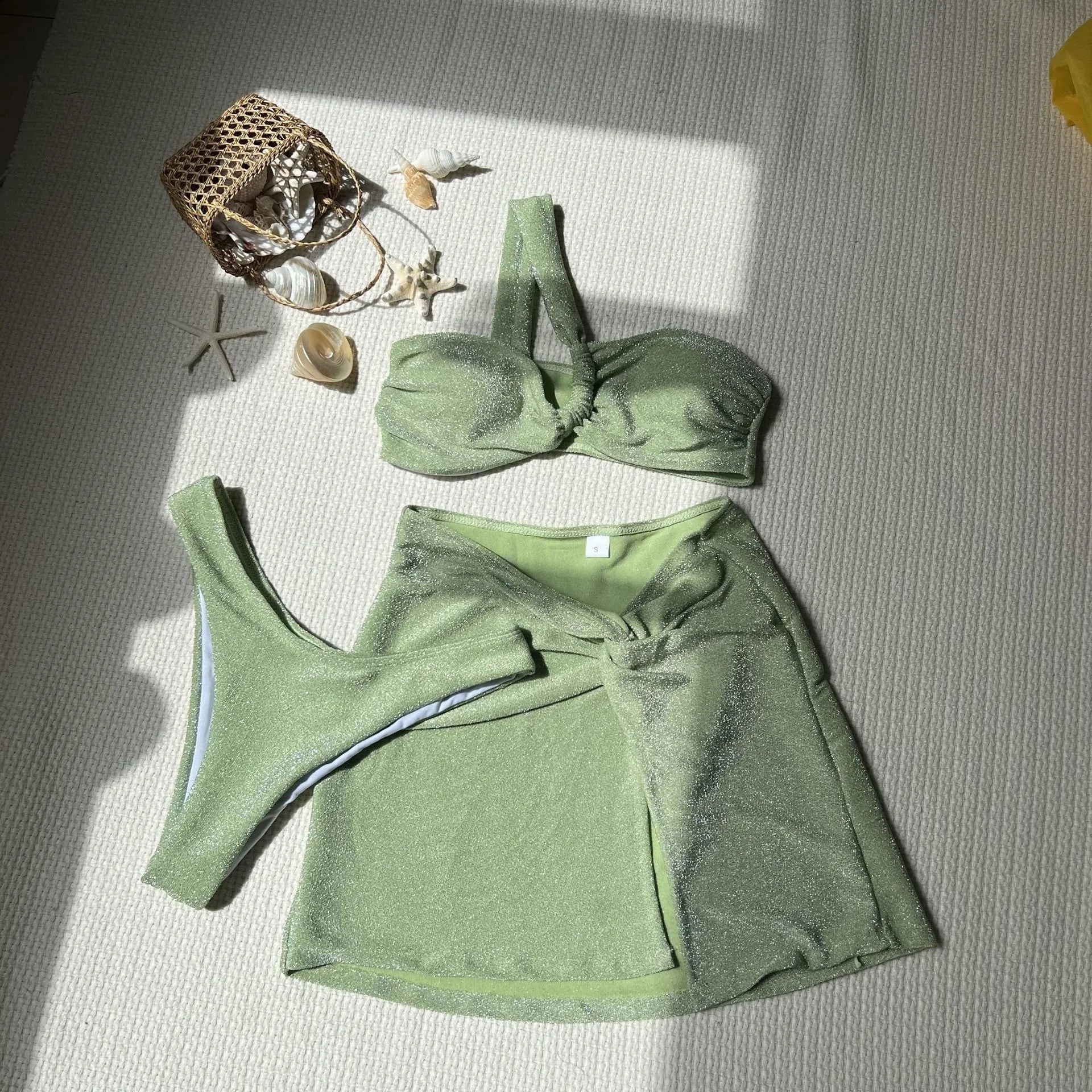 Women's light green one-shoulder swimsuit with matching bottoms and skirt on a white background.