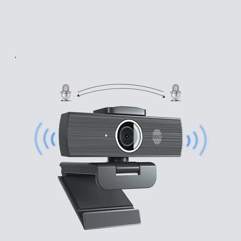 Black USB computer webcam with a magnetic privacy cover on a desk next to a laptop