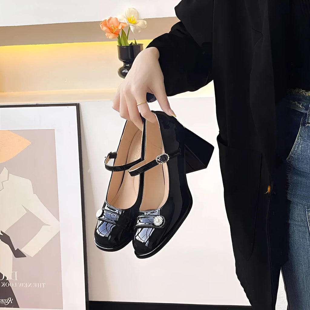 Women's black patent leather round toe shoes with a chunky block heel and buckle fastening.
