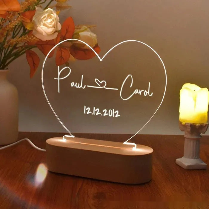 Custom transparent acrylic LED night light engraved with personal names and a date on a bedside table.