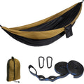 Green and black double parachute cloth hammock hung between two trees with attached ropes and buckles.