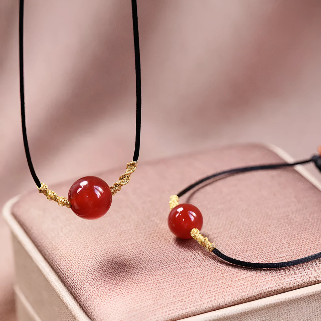 Hand-woven red agate bracelet and necklace set with bean-shaped beads on a textile background.