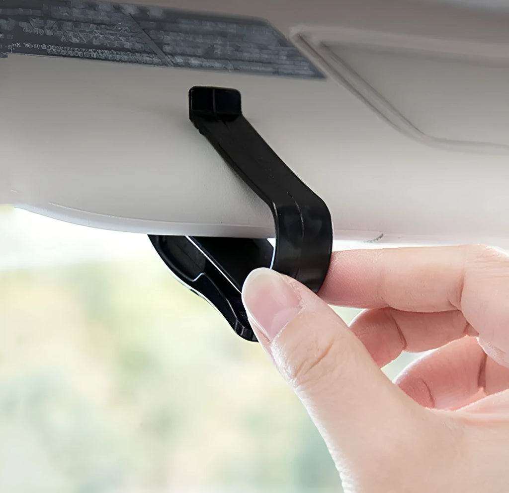 Black plastic clip mounted on a car sun visor holding a pair of sunglasses and an ID card.