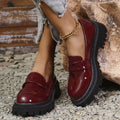Black slip-on loafers with a chunky platform heel and thick rubber sole on a wooden floor.