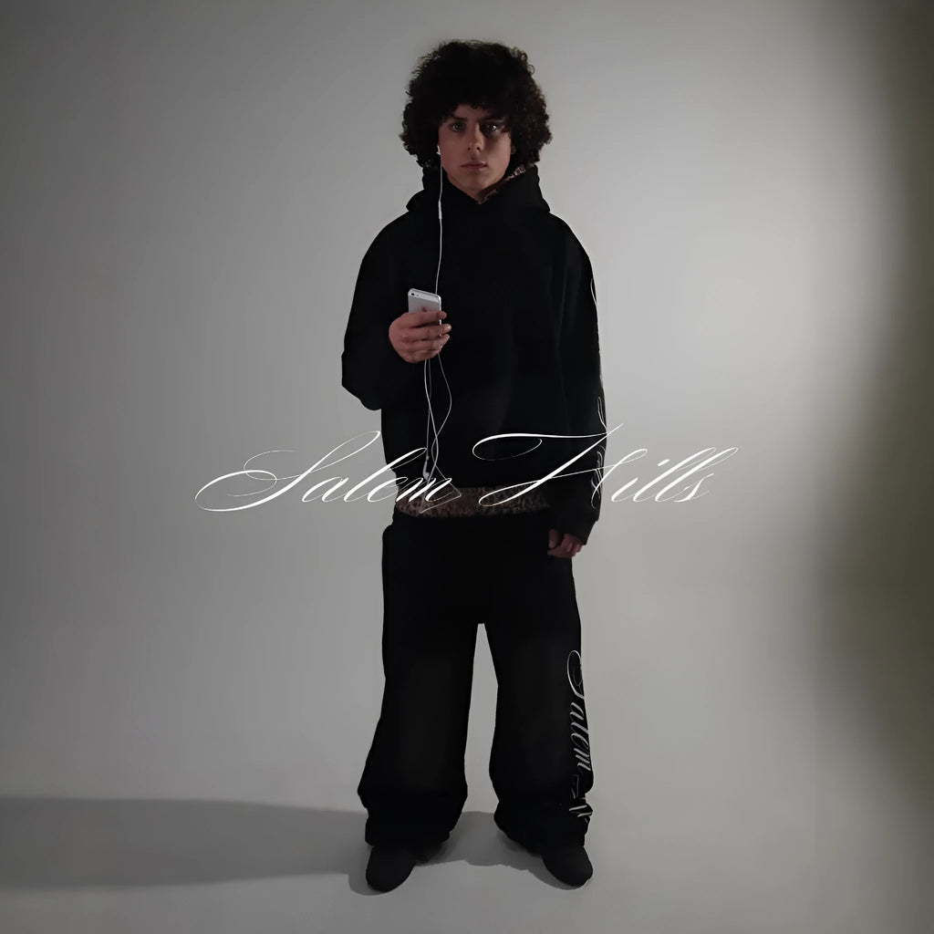 Man wearing a black punk-print hooded pullover jumpsuit with long sleeves and fleece lining.