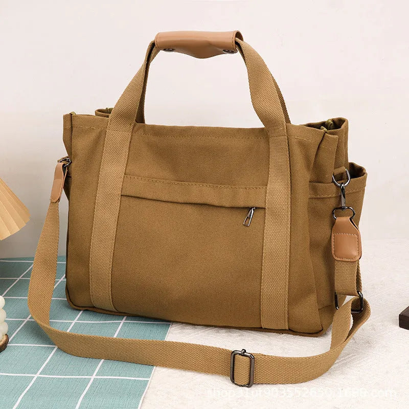 Khaki canvas tote bag with zipper closure showing internal camera pocket and document bag compartments.
