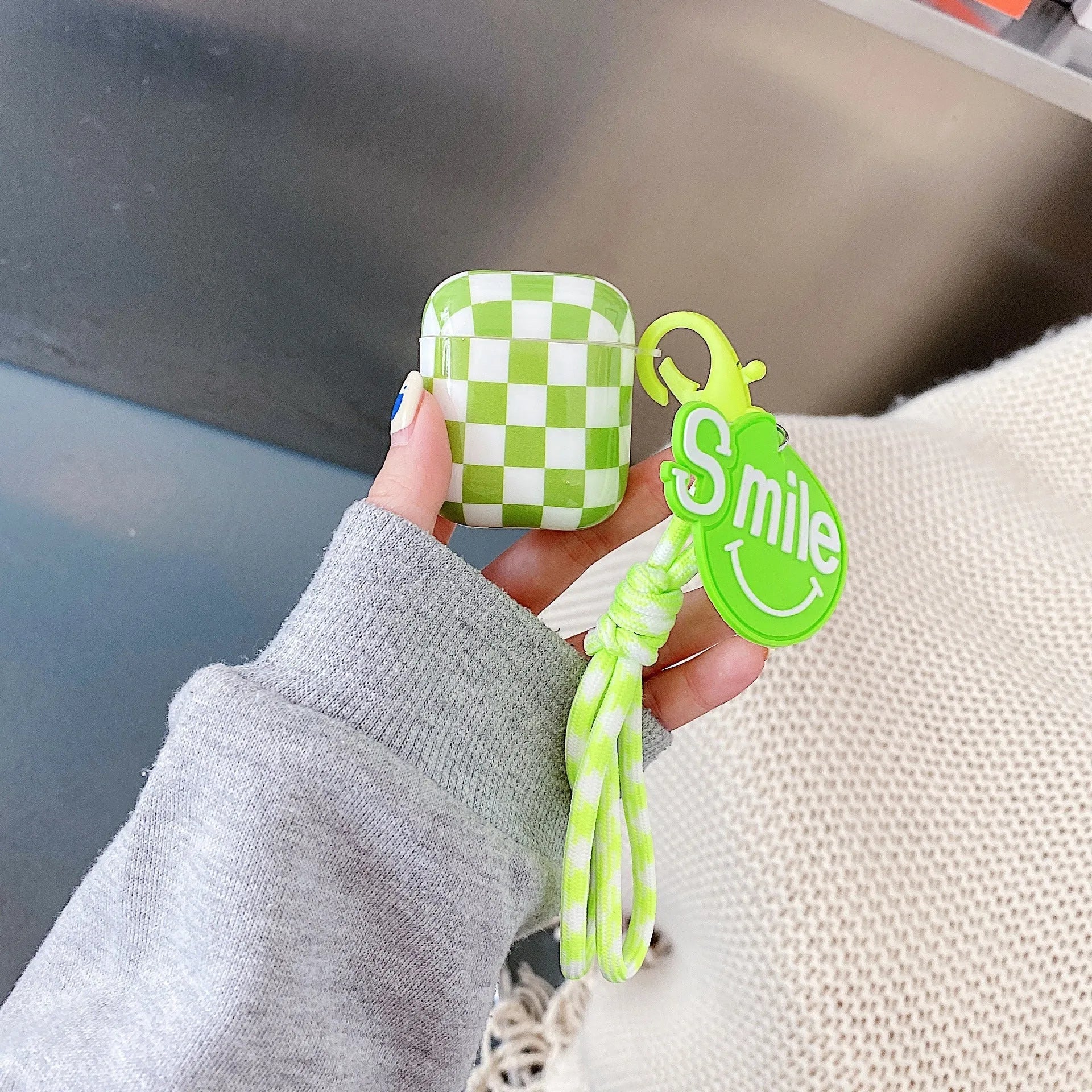 Black and green checkerboard pattern TPU protective case covers for Apple AirPods, one with a smiley face lanyard.