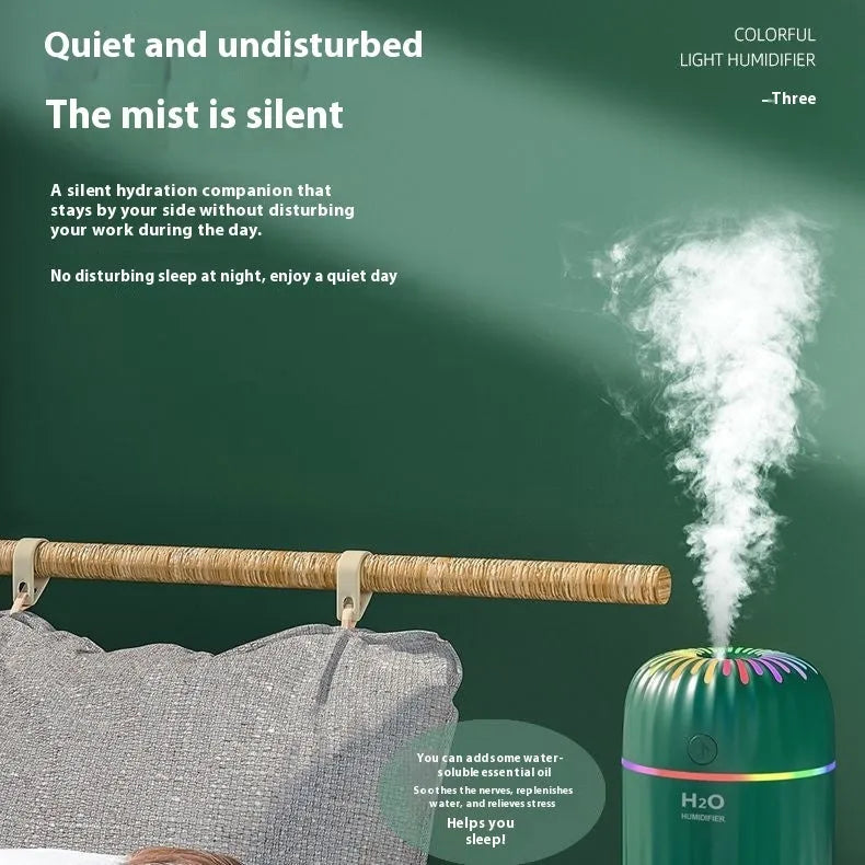 A green USB mini car aromatherapy humidifier on a desk next to a laptop, showing its compact size.
