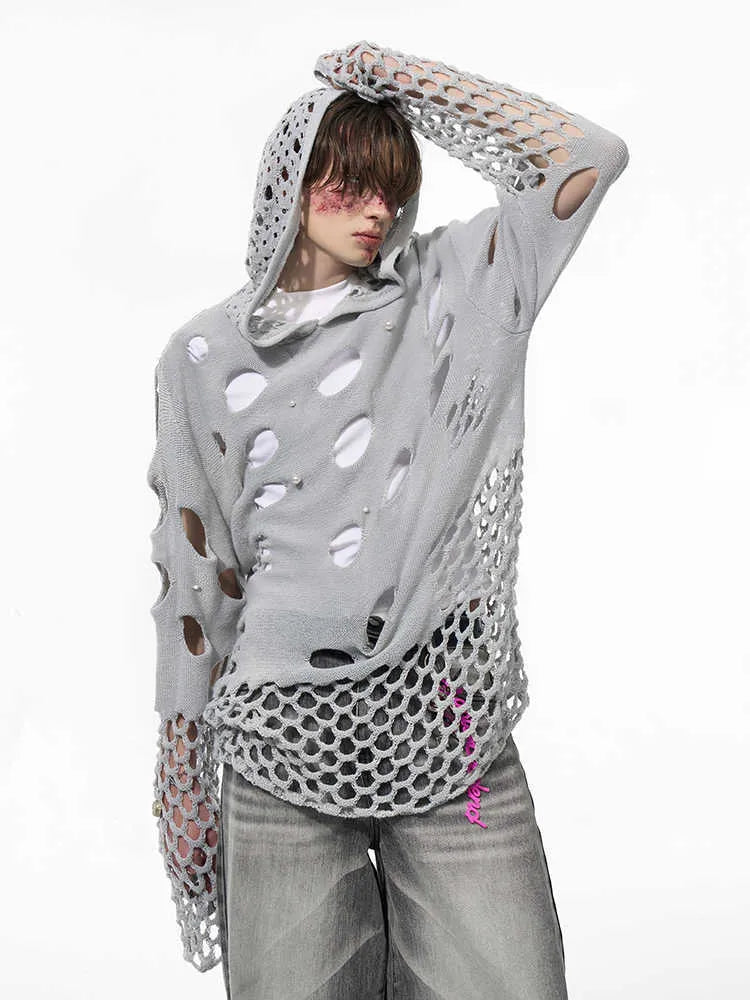 Man wearing a loose black hoodie with a pearl decoration on the front of the hood.