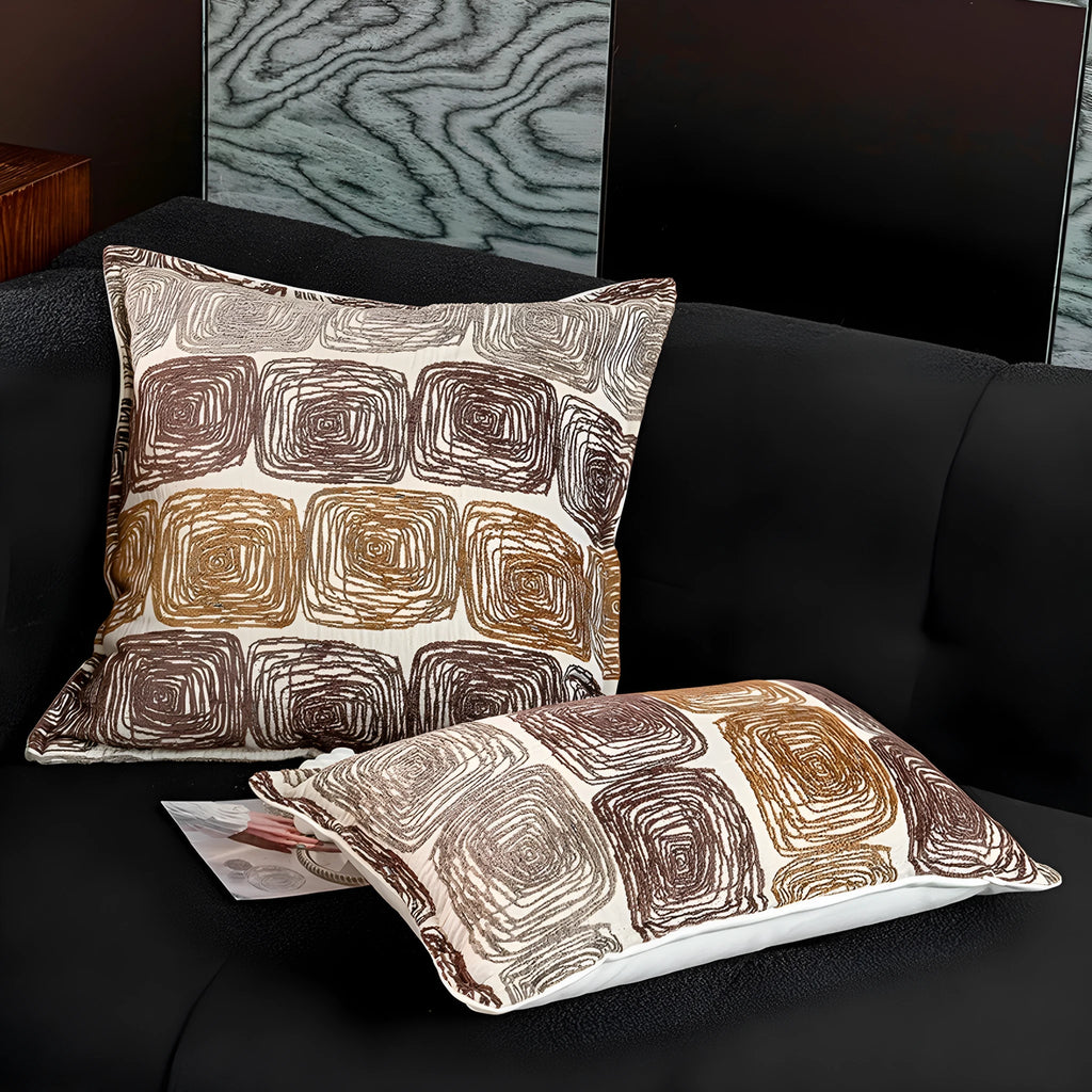 Cream and coffee-coloured abstract coil pattern square pillow cover 50x50cm on a grey sofa.
