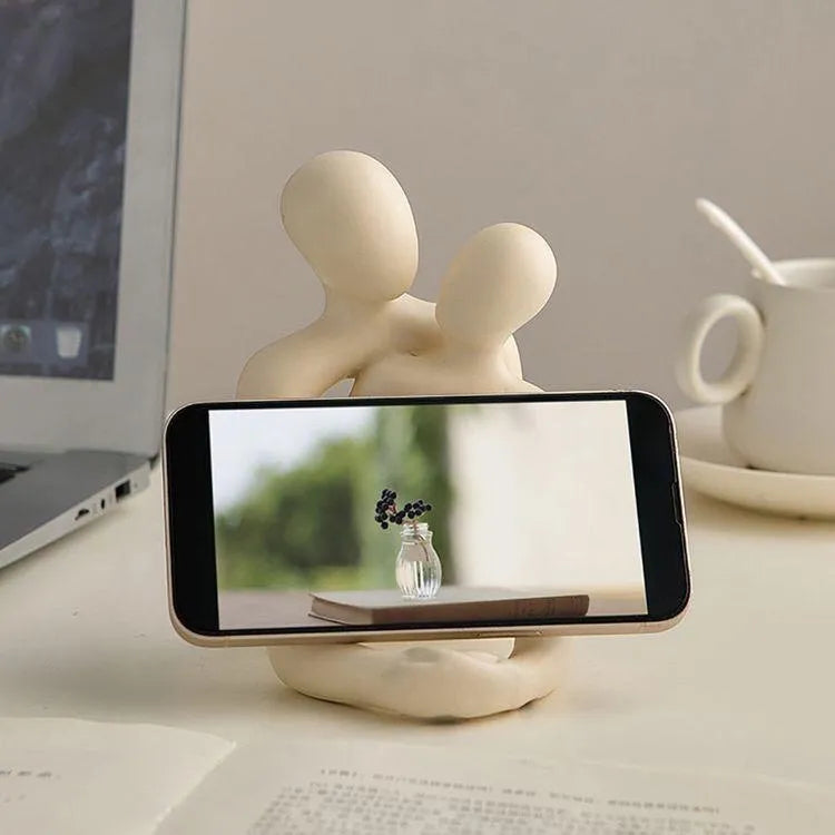 Modern resin sculpture of an embracing couple in milky white or gold finish on a wooden surface.