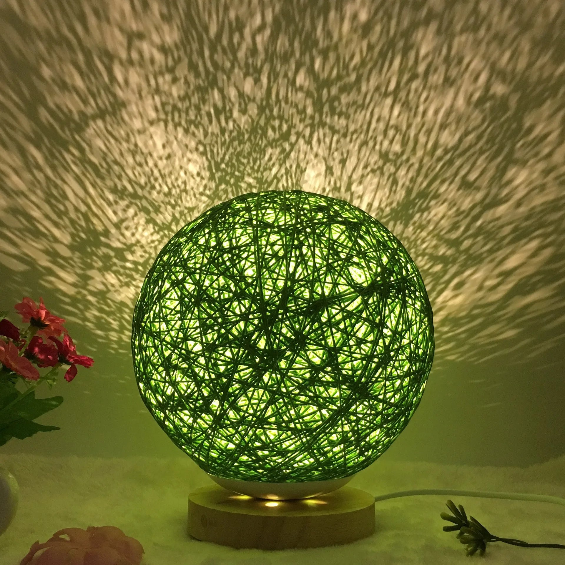 White hand-knit linen rattan ball table lamp with remote control on a wooden bedside table.