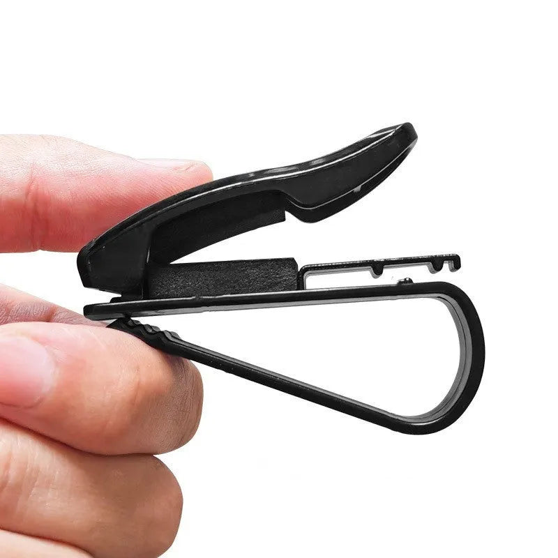 Black plastic clip mounted on a car sun visor holding a pair of sunglasses and an ID card.