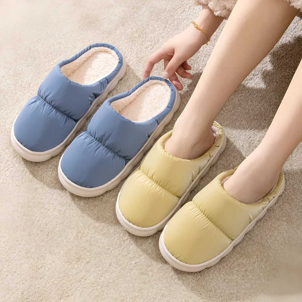 A pair of thick-soled house slippers with an artificial leather upper and plush lining, shown in a choice of colours.
