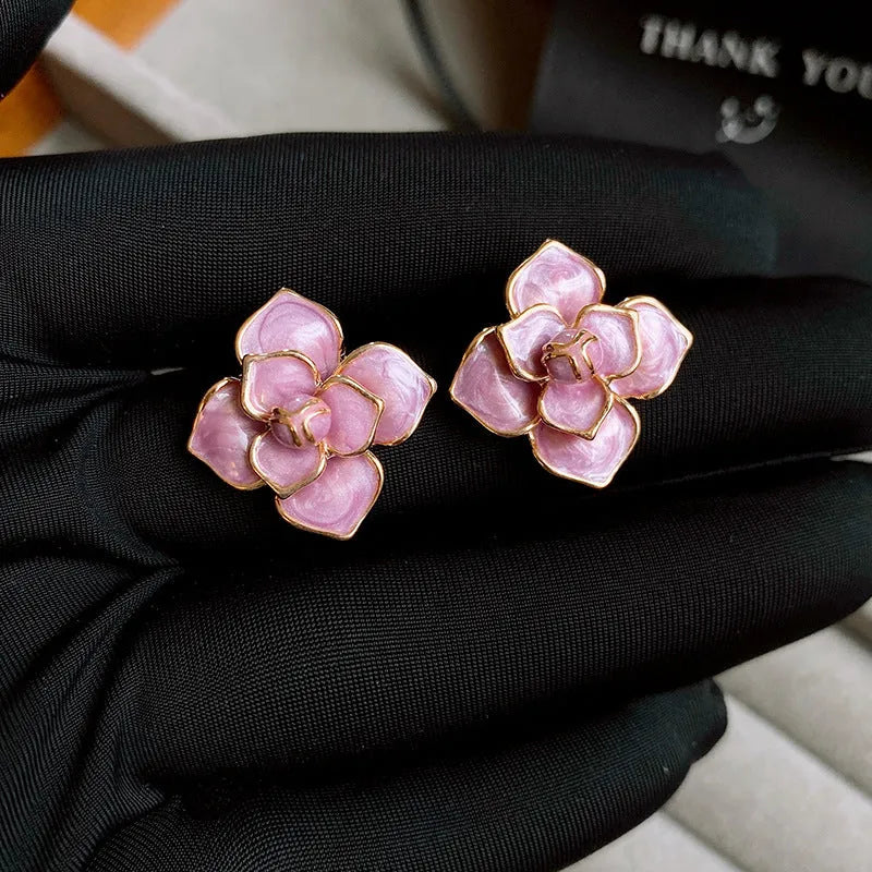 A pair of gold-plated purple floral stud earrings with silver needle details on a white background.