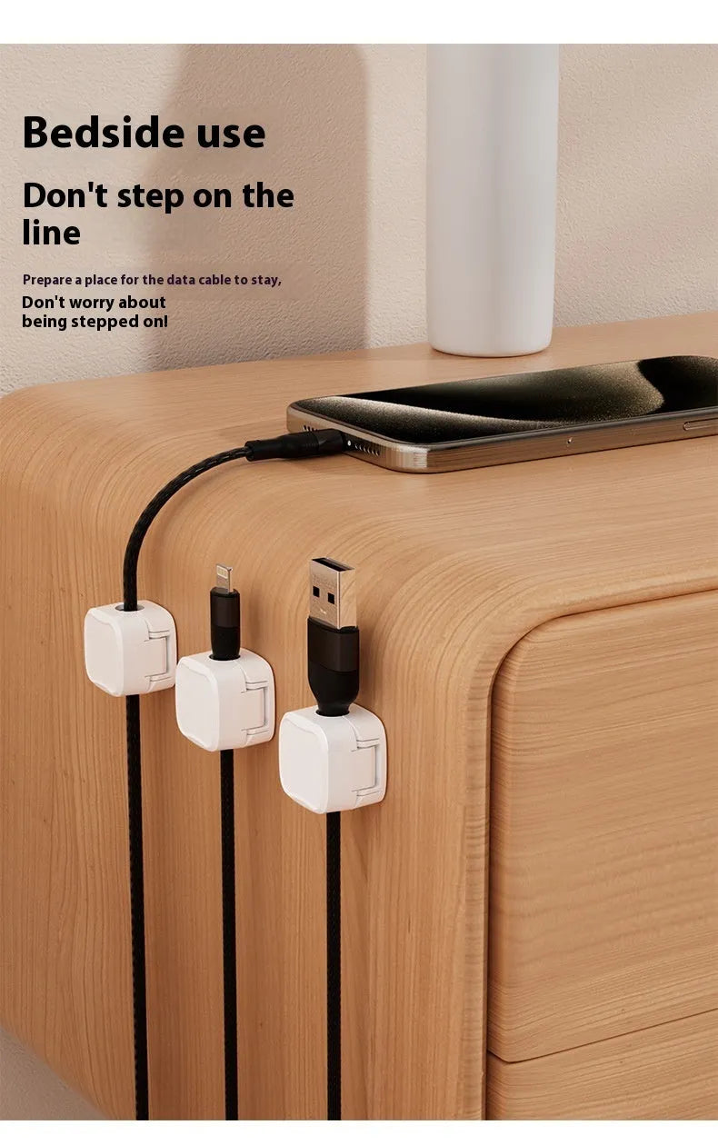 White and black magnetic adhesive cable clips holding a USB cable against a wooden desk.