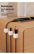 White and black magnetic adhesive cable clips holding a USB cable against a wooden desk.