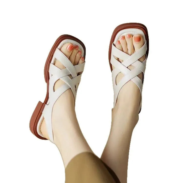 Women's glossy black patent leather sandals with square toe and cross-belt fastening on a light background.