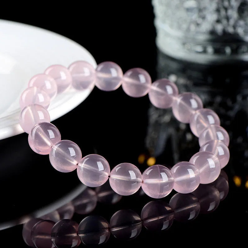 A pink natural crystal bead bracelet with polished round beads in a single circle design on a wrist.