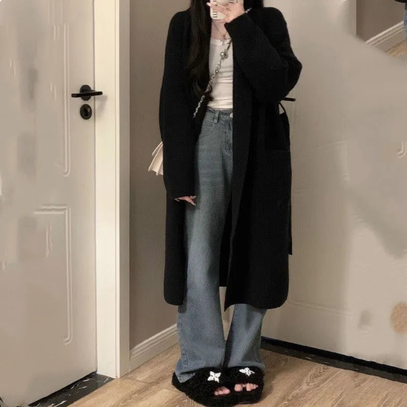 Woman wearing a loose, thick dark gray knitted cardigan with a 3D pattern and long sleeves.