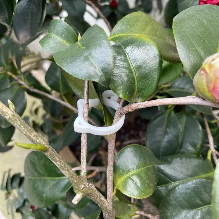 Red plastic cat-shaped clip for holding plant stems, shown against a green leaf background.