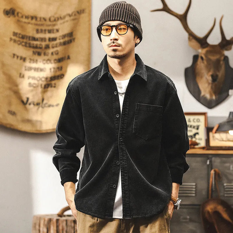 A man wearing a loose-fit black corduroy shirt jacket with long sleeves.