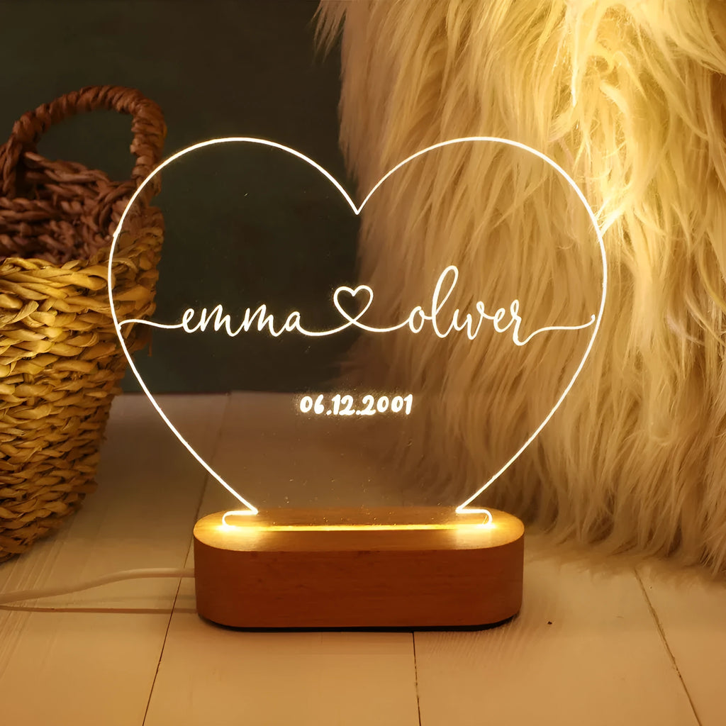 Custom transparent acrylic LED night light engraved with personal names and a date on a bedside table.