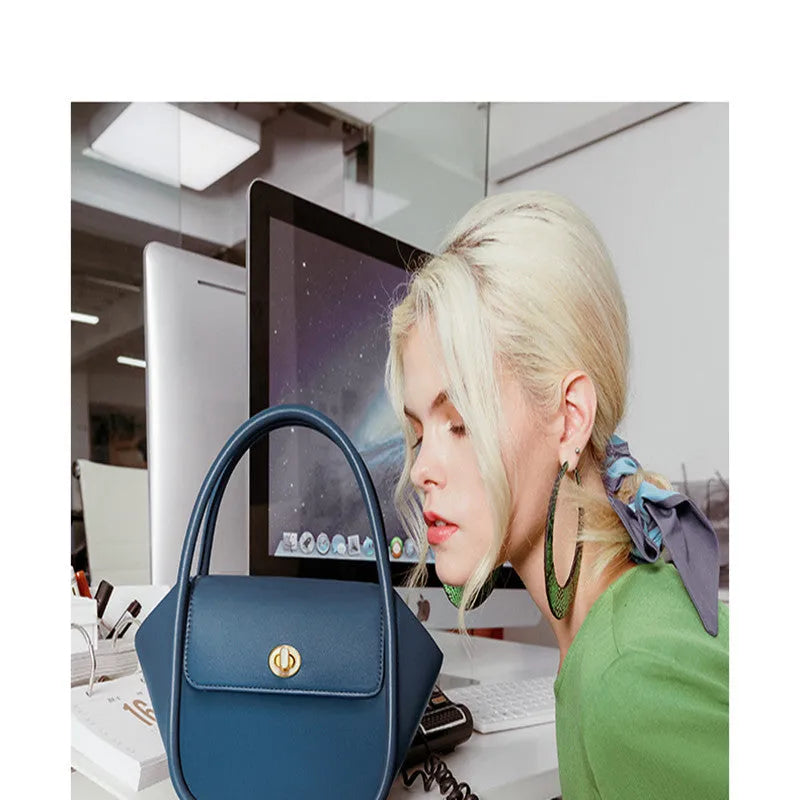 Women's wing-shaped leather tote bag with a latch buckle, shown in Atlantic blue with a cross-body strap.