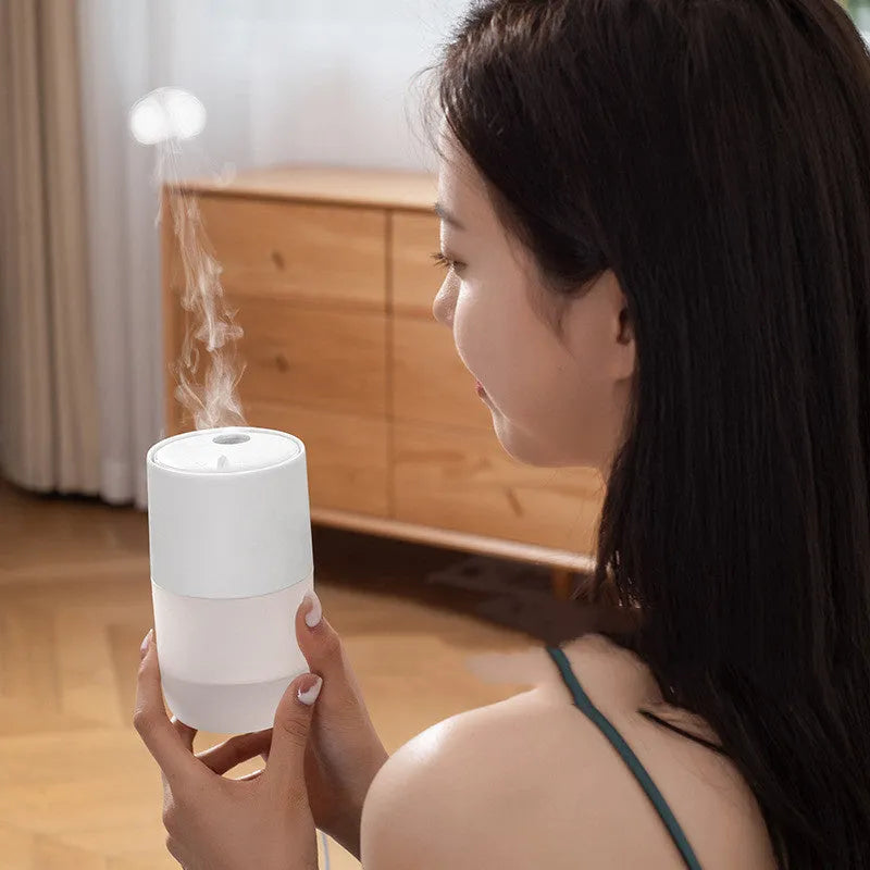 Mini portable jellyfish-shaped ultrasonic humidifier in black, with USB cable and essential oil bottle on a desktop