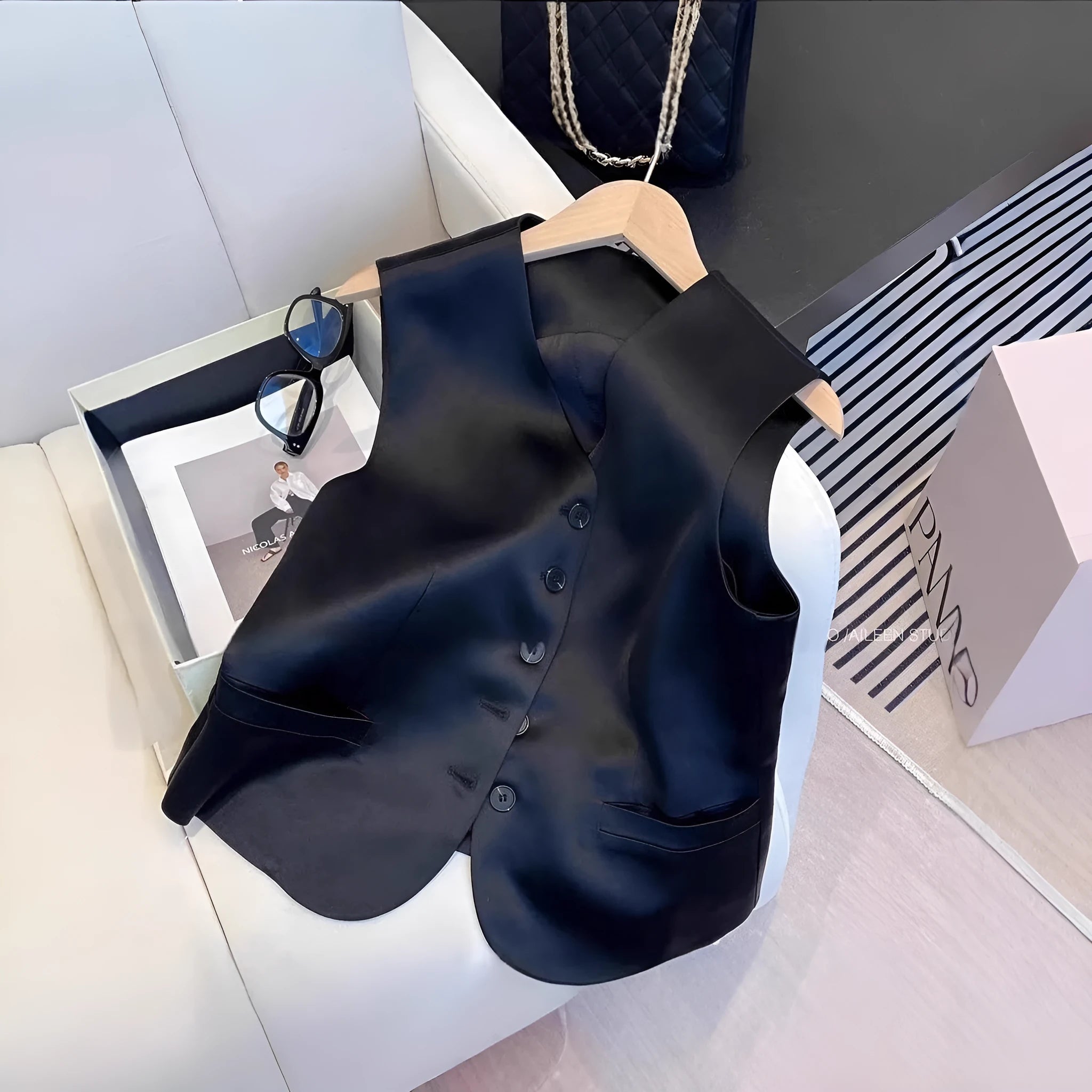 Black satin ladies' sleeveless vest with loose fit and splicing detail on a hanger.